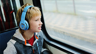 Boy on autism spectrum wearing blue headphones looking out of train window