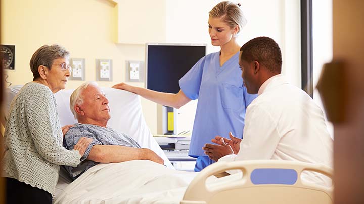 Medical Team Meeting With Senior Couple In Brightly Lit Hospital Room